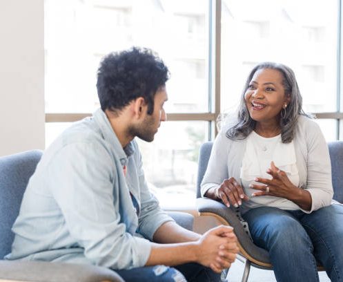 The senior adult female counselor gestures and talks excitedly about the progress the young adult man has made.